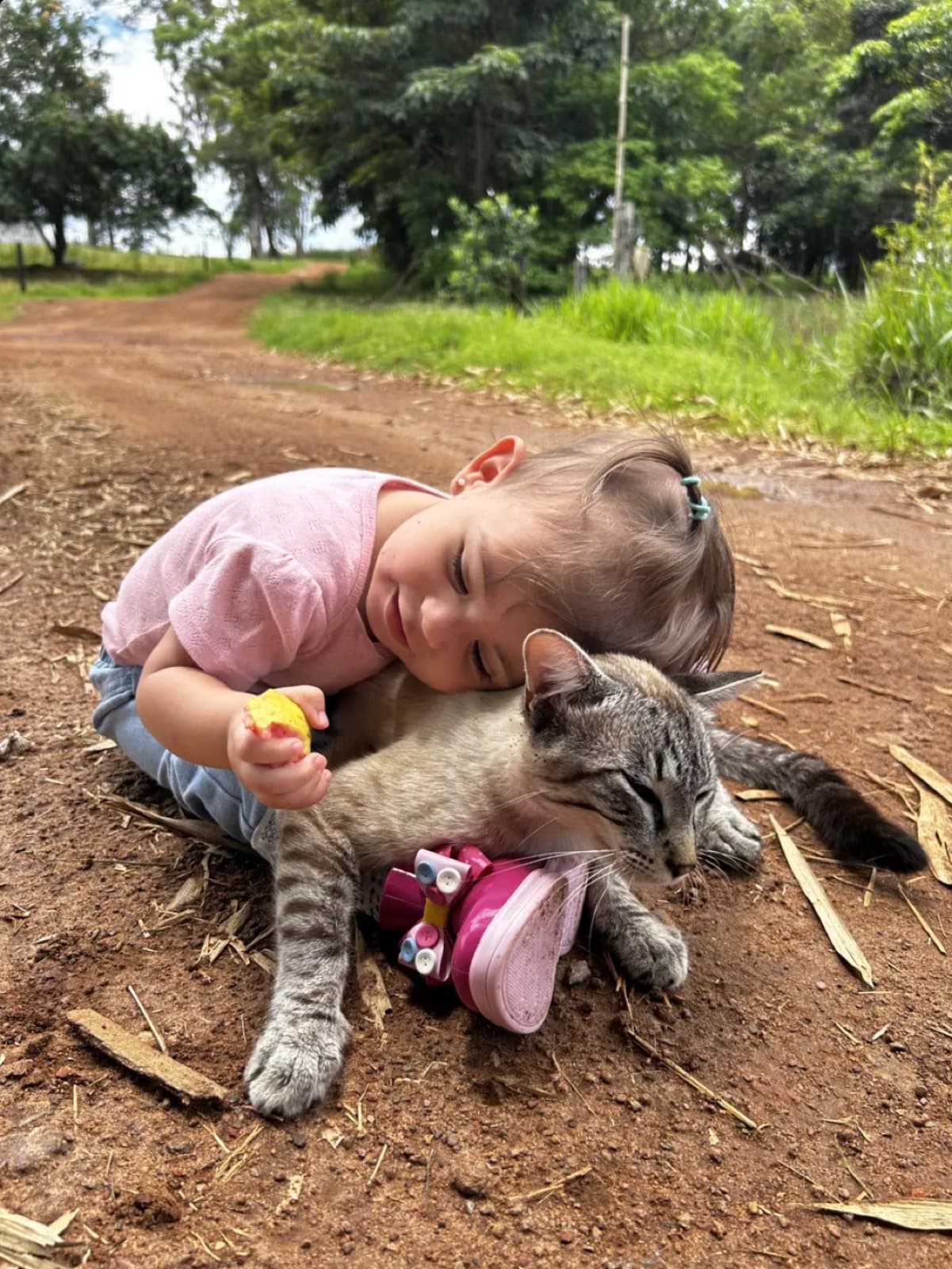 Lara deitada abraçando um gatinho na estrada de terra